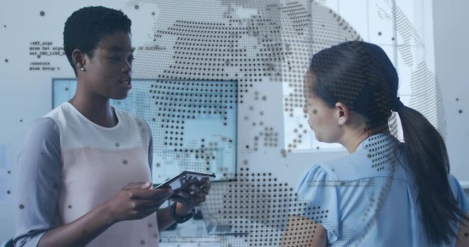 Vertical video: Starting tablet, two women in pink blue tops sharing checking plans at office globe
