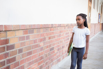 African American schoolgirl walking along brick hall holding green and yellow notebooks, copy space