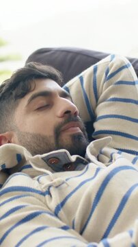 Vertical video: Resting man breathing on couch by big window sunlight lulling rest in cream sweater