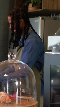 Vertical video: Taking phone barista at counter olive apron tapping POS selling pastry