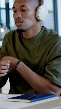 Vertical video: Massaging man wearing green tee and white headphones feeling arm stiffness at desk