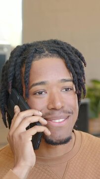 Vertical video: Taking call man with locs in sweater holding phone to left ear at office talking