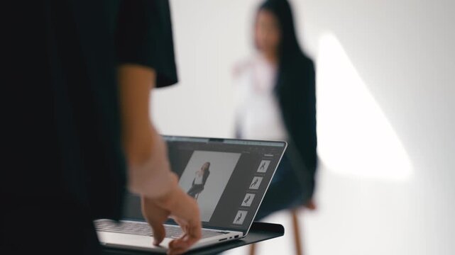 Photographer retouches photos on a laptop with editing software in a bright studio with a model in the background
