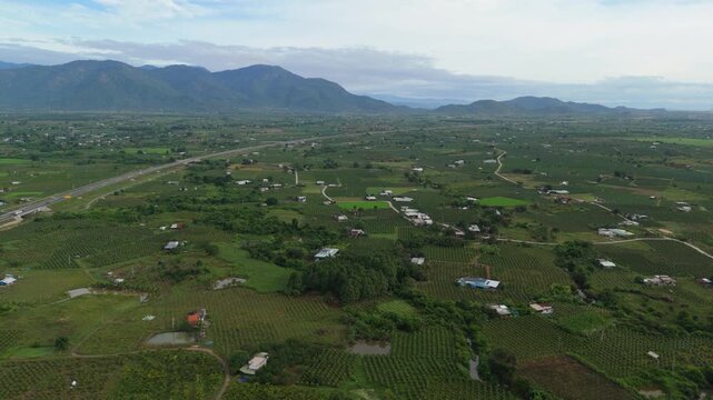 Aerial drone view of vast countryside farmland with scattered houses and mountains under cloudy sky