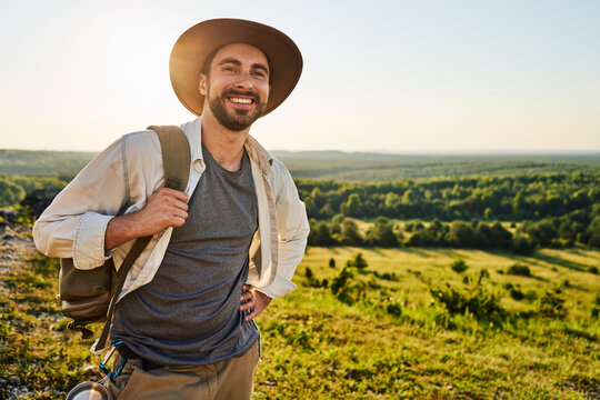 Happy young bearded male hiker smiling confidently on hilltop with lush green valley