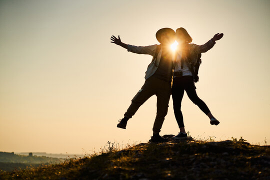 Joyful couple on hilltop at golden sunset with arms outstretched in celebration