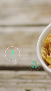 Popping teal icons drifting across blurred wood, cornflakes bowl right, recycle plug, copy space