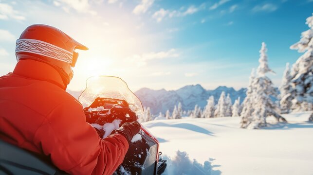 A snowmobiler dressed for the winter, enjoying the breathtaking snow-covered landscape with mountains and trees bathed in a warm golden sunlight at sunset.