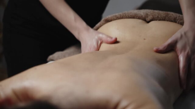 Female massage therapist applies pressure to the back of a client during a therapeutic session in a serene indoor environment with soft lighting