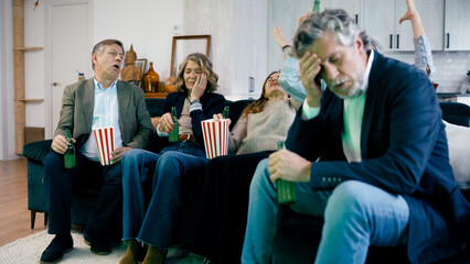 Senior friends watching a losing sports match on television, showing disappointment and sadness....
