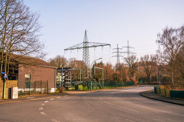Obraz premium Empty asphalt road leading to a power substation and high voltage towers at sunset