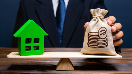 Green house and money bag balanced on wooden scale