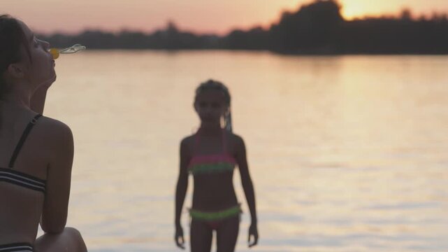 Funny girl catches bubbles on the shore of the lake, which her older sister lets go
