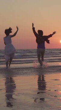 Vertical Screen : Young Asian people running on beach to the sea, friends happy relax having fun playing on beach near sea when sunset in evening. Lifestyle friends travel on beach concept.