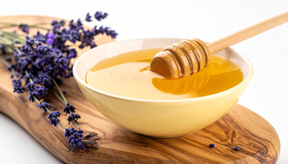 Golden liquid honey in a pale yellow bowl with a wooden dipper and lavender sprigs on a rustic