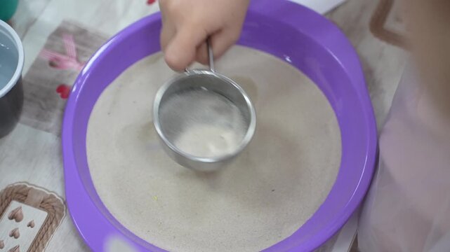 A child at a master class sifts sand through a sieve in close-up. High quality video