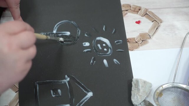 The child and the mother paint the paper with glue to fill the drawing with sand. Developing master class