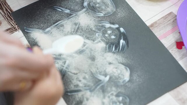 The child and the mother paint the paper with glue to fill the drawing with sand. Developing master class