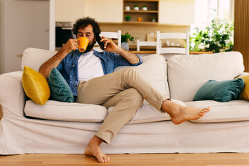 Fototapeta premium Man drinking coffee while talking on smartphone at home