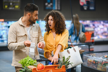 Couple checking long grocery receipt experiencing financial shock