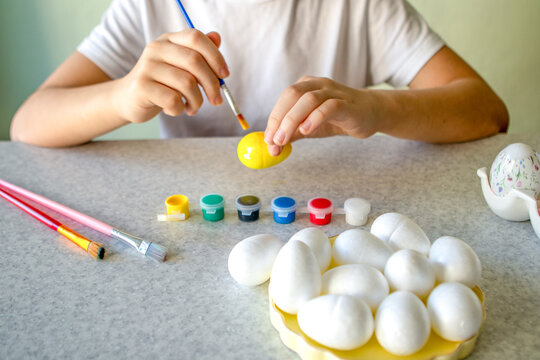 Child painting a yellow Easter egg at home, creative spring craft