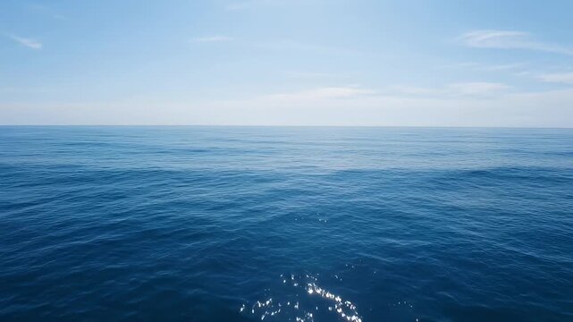 Calm blue ocean under a bright sky with scattered clouds reflecting sunlight