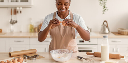 A person is breaking eggs into a bowl in a kitchen. Ingredients like flour and milk are nearby. The...
