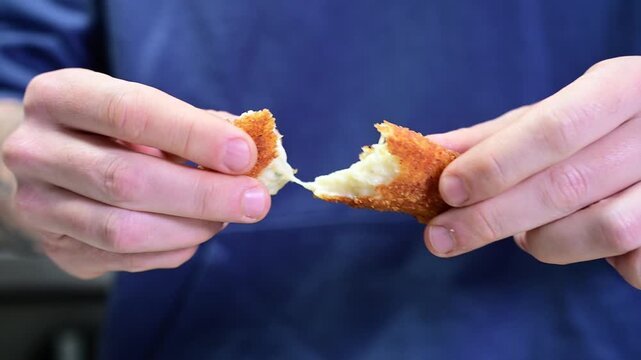 Close-up of chef's hands breaking a potato croquette in half in a restaurant kitchen