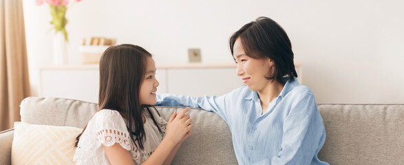A mother and daughter sit on a couch in a living room. They are talking and enjoying their time...