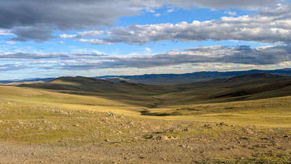Obraz premium Vast Rolling Steppe Landscape in Mongolia Under Dramatic Cloud Sky at Sunset
