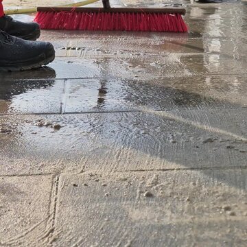 Low angle super slow motion of water jet and wet sand being swept into paving stone joints.
