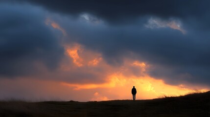 Fototapeta premium A solitary silhouette stands on a hill against a dramatic sky ablaze with sunset colors