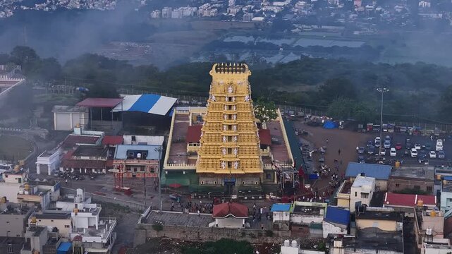 Cinematic drone view of golden Sri Chamundeshwari Temple atop Chamundi Hills on misty day