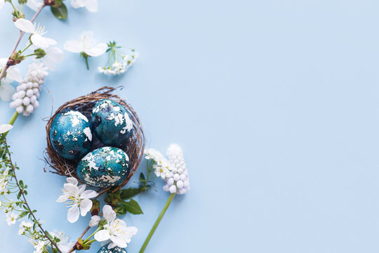 Easter flat lay. Stylish easter eggs in nest and cherry flowers on blue background. Easter celebration, season greetings mockup. Spring modern floral banner