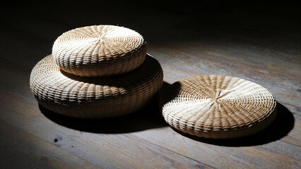 Three Woven Bamboo Floor Cushions Stacked and Placed on Rustic Wooden Floor Illuminated by Dramatic Spotlight Creating Soft Shadows for Interior Decor or Meditation Space