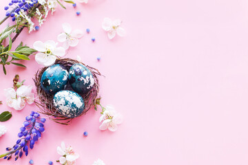 Easter flat lay. Stylish easter eggs in nest and cherry flowers on pink background. Easter celebration, season greetings mockup. Spring modern floral banner © sonyachny