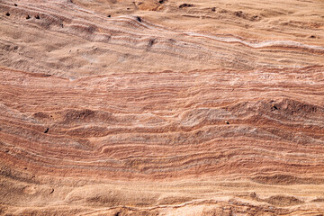 Natural layered sandstone rock surface with visible sediment lines and erosion patterns. Warm desert earth tones creating abstract geological texture background.
