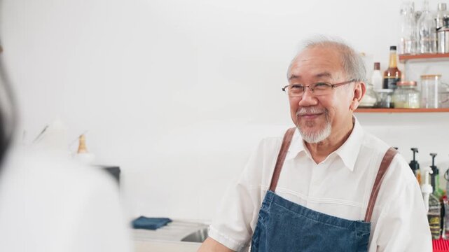 Friendly senior Asian male barista holding a paper cup and asking a customer if they want their coffee to go. Excellent service, takeaway options, and hospitality in a modern cafe