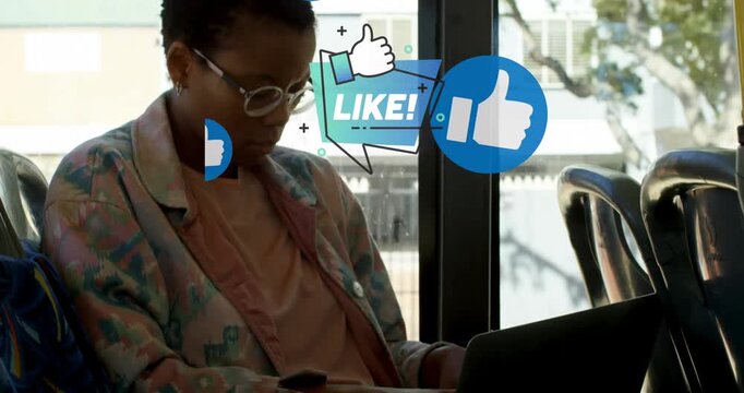 Multiple thumbs up icons floating against african american woman using laptop in the bus