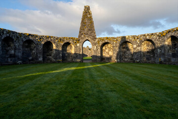 Obraz premium Ancient Stone Monastery Ruins with Arched Walls and Central Tower Standing Amidst Vibrant Green Lawn under Dramatic Sky