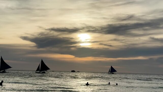 Silhouetted sailboats and people enjoying the calm sea during a beautiful and serene golden hour, tc01