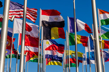 Colorful national flags waving on tall flagpoles under a deep blue sky, conveying international unity, patriotism, diplomacy and cultural diversity at a public display or event. Doha, Qatar 