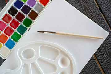 Watercolor painting setup with tools on a wooden table in a bright outdoor space during daytime