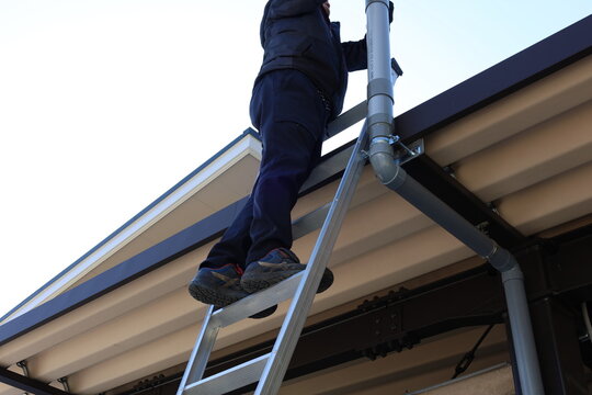 Man on a ladder inspecting home roof and gutters