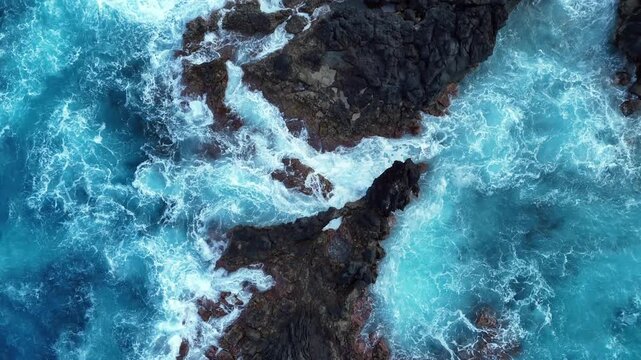 Stunning Overhead Aerial View of Dark Volcanic Rock Surrounded by Electric Turquoise Pacific Ocean
