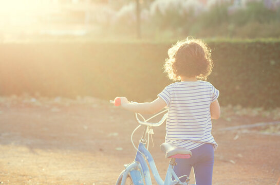 Rear view of a Girl in casual clothing walking along a dirt road with her bicycle