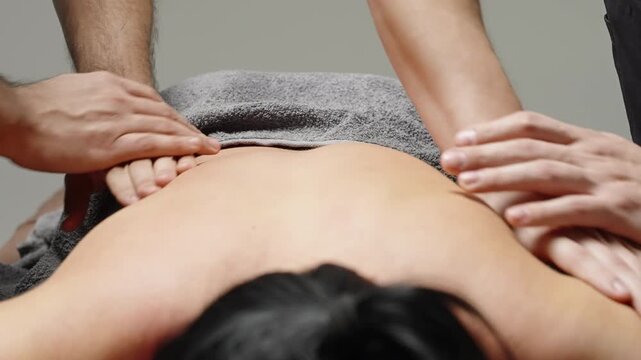 Two therapists perform a synchronized four-hands back massage, kneading shoulders and upper back to deliver relaxation and muscle relief during a calming wellness treatment.