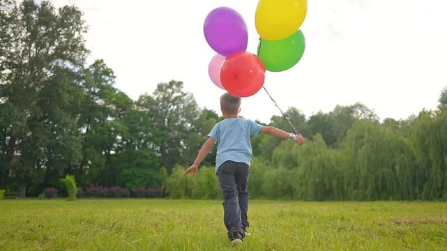 Boy runs with colorful balloons in field. Child plays outdoor with balloon bunch. Happy kid running on grass. Summer childhood fun with balloons. Boy holds balloon string while playing outdoor.