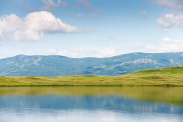 Fototapeta premium Green mountains with trees and the blue sky with clouds are reflected in the lake.