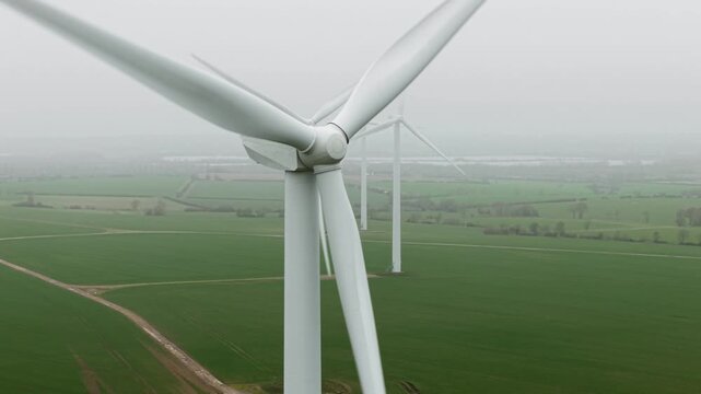Aerial drone view of a massive wind turbine farm in a rural UK landscape surrounded by thick fog and low clouds